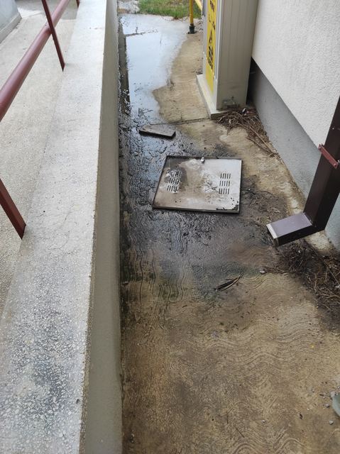 Spațiu îngust între un zid de sprijin și peretele blocului, cu apă pe jos