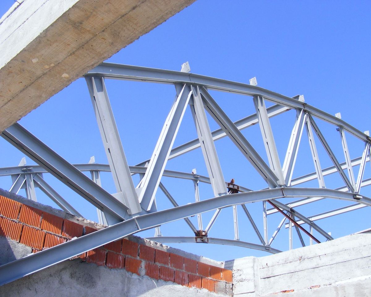 Arc metalic cu zăbrele al unei săli de sport, văzut de jos, pe cer albastru