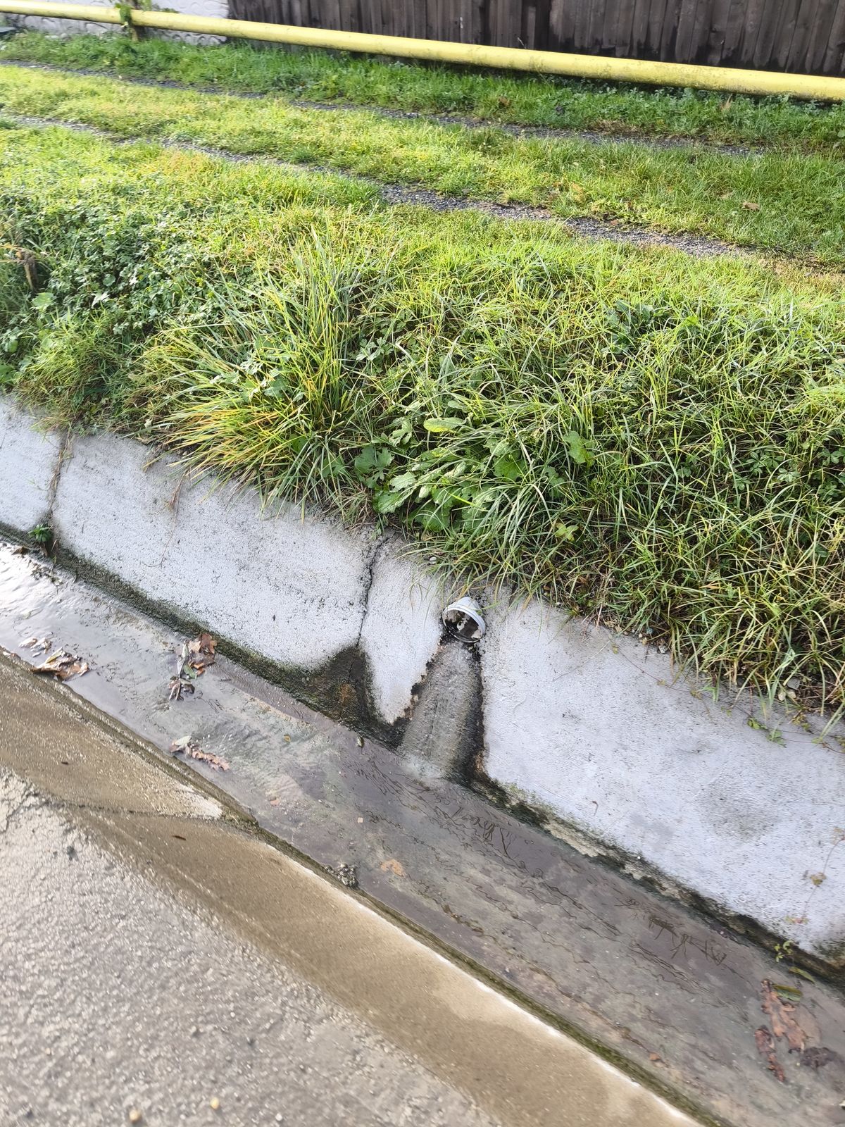 Zid de sprijin scund din beton, cu o barbacană prin care curge apă spre rigolă