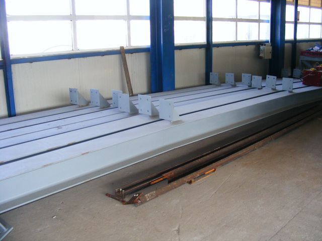 Profile metalice vopsite, așezate în șir într-o hală de producție