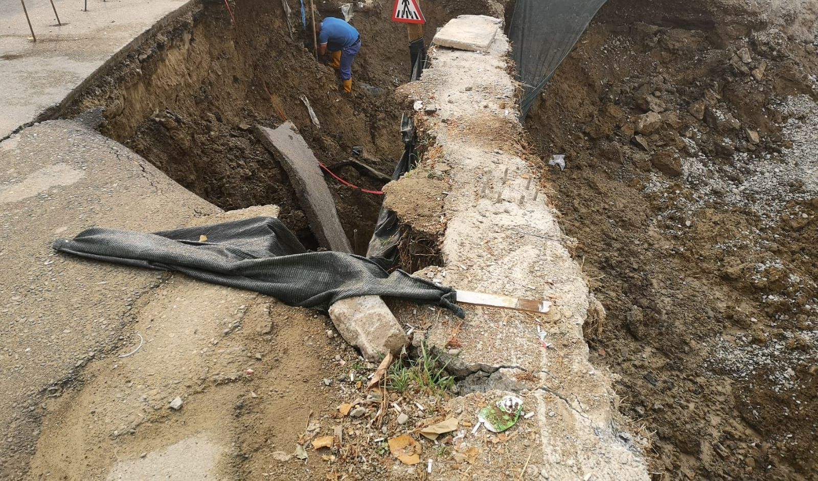 Margine de carosabil prăbușită în groapa de fundație vecină, cu o conductă ruptă și folie de protecție