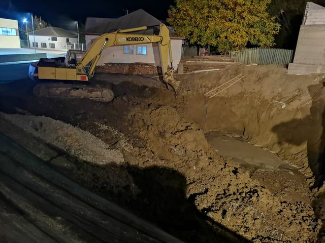 Excavator galben în groapa de fundație, noaptea, cu apă pe fundul gropii