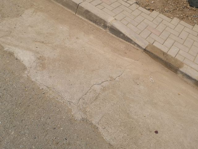 Dală de beton cu fisuri fine, lângă bordura unui trotuar pavat