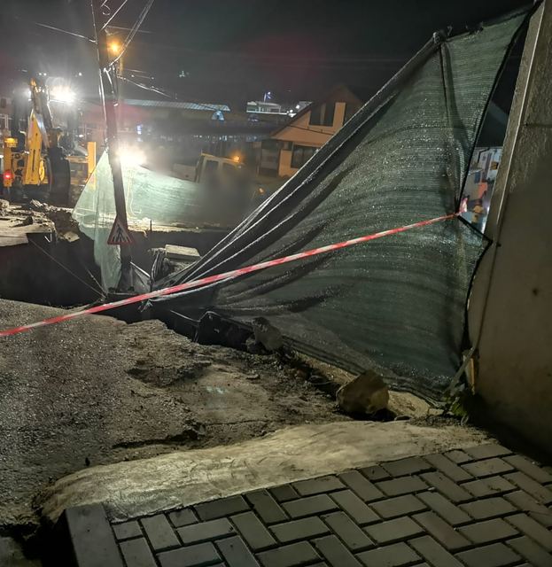 Stradă surpată, îngrădită cu bandă și plasă, noaptea, cu un utilaj în fundal